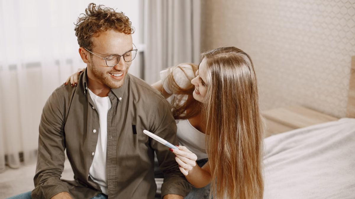 Joyful couple sitting on bed, holding a pregnancy test, embracing new beginnings.